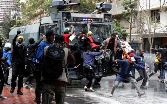 People jump in front of and on large, armored vehicle in street. 