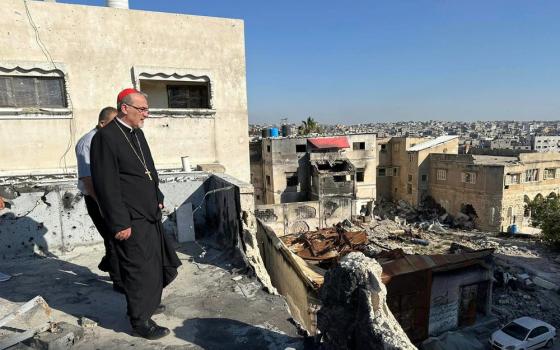 Pizzaballa stands on rooftop surveying vast ruins; the cardinal wears plain black clericals, with a red zucchetto.