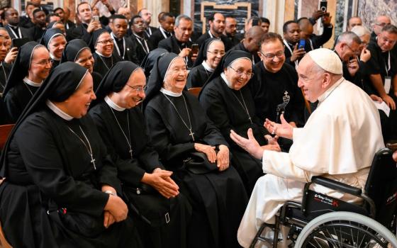 Pope, in wheelchair, sits very near group of habited sisters who all laugh in response to pope's comment. 