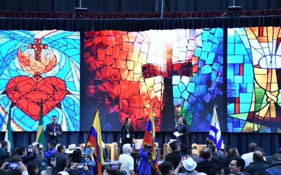 People stand on stage; behind stage are illuminated panels of mosaic-style images. 