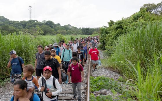 Long line of people walks down track surrounded by tallgrass.