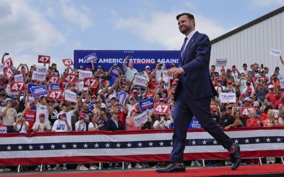 Vance walks across red-carpeted platform; in background, supporters in stands hold signs.