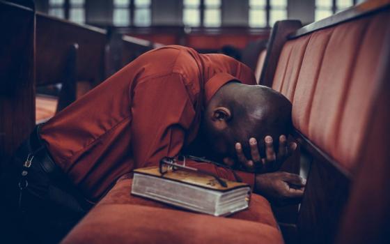 Man with head down on chairs, praying