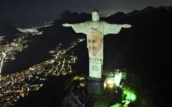 Pope Francis' face projected at night onto monumental statue. 