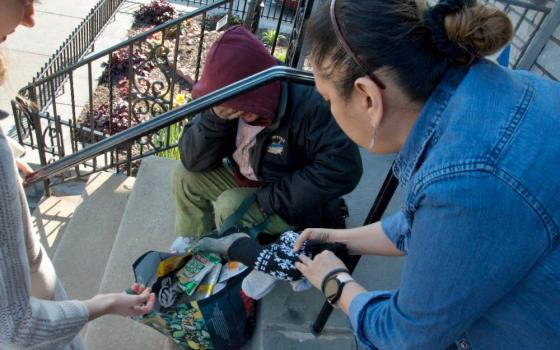 Sisters of St. Joseph Welcome Center Executive Director Olivia Sharkey, left, and a staffer offer warm gloves and a hat to a neighbor suffering from the cold March air outside the center in Philadelphia's Kensington neighborhood. (GSR photo/Dan Stockman) 