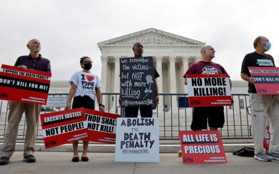 5 people stand in front of Supreme Court building holding signs. 