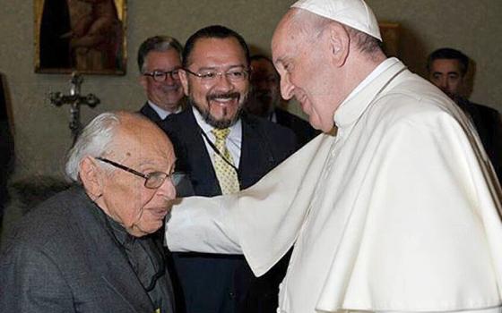 Francis smiles and puts his hand on Gutiérrez's shoulder. Gutiérrez is seated.