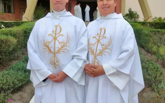 Arcos poses for picture next to other pries; both wear white chasubles.