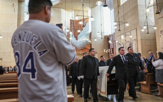 In foreground is back of fan wearing Valenzuela jersey, centered are pall bearers carrying casket through Cathedral aisle. 