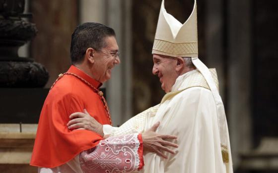 The cardinal embraces the pope, who is vested for Mass in white, wearing mitre.