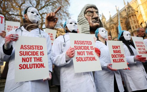 Masked protesters wear white medical coats and hold signs reading "Assisted suicide is not the solution."