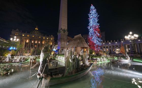 Illuminated tree and Vatican obelisk visible in background; foregrounded is part of nativity scene. 