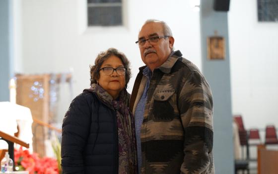 Older couple standing side by side, arms around each other.