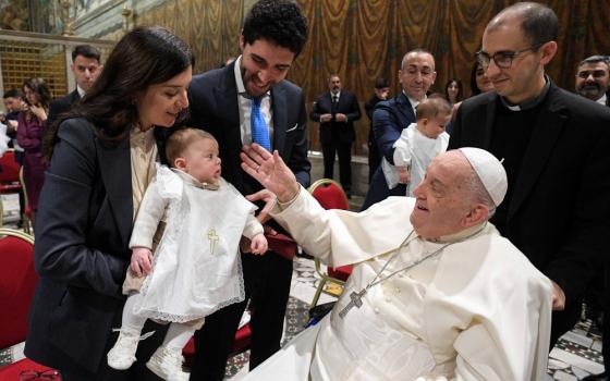 Pope seated in wheelchair, smiles at baby.