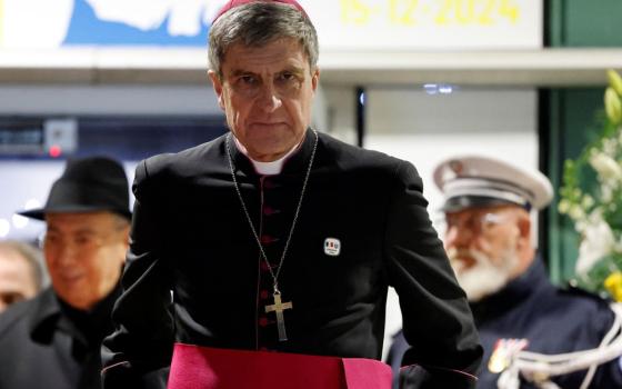 The archbishop seen in black cassock trimmed with purple walking with solemnity.