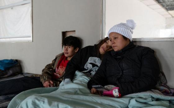 Mendez and children wear winter clothing and sit together beneath blanket.