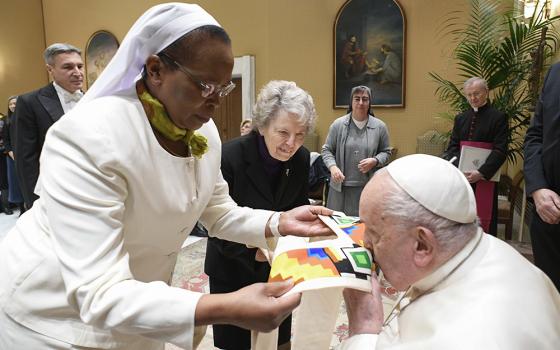 Pope Francis kisses a gift presented to him by Sr. Jane Wakahiu during an audience with the board of directors of the Conrad Hilton Foundation at the Vatican on Jan. 22. Standing to the right is Sr. Joyce Meyer, a member of the Presentation of the Blessed Virgin Mary, and member of the foundation's board of directors. (CNS/Vatican Media)