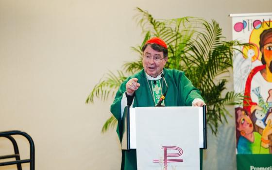 Cardinal Pierre vested for ordinary time stands at ambo gesturing and speaking.