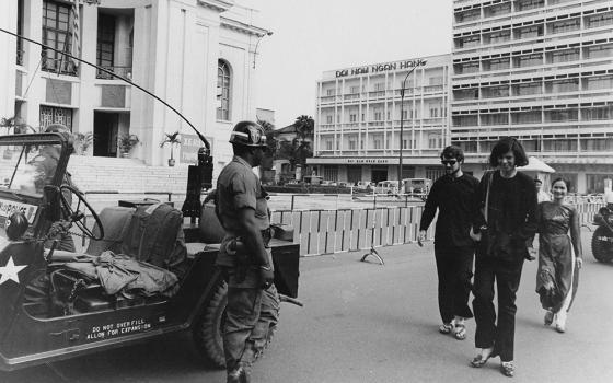 Tom Fox; Gloria Emerson, a correspondent for The New York Times; and Hoa Fox walk through downtown Saigon circa 1972, dressed in traditional Vietnamese farmer attire — which were often mistakenly identified as Viet Cong uniforms — while wary U.S. Military Police observe from a distance. (Courtesy of Thomas C. Fox)