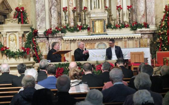 The bishops sits at table in front of altar.