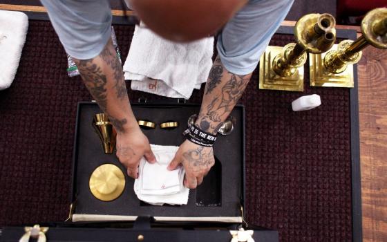 Only the inmate's arms and hands are visible, from above, folding a small altar cloth.