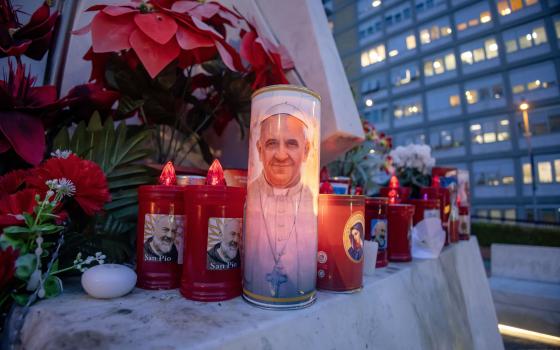  Votive candles and flowers are seen at the base of a statue of St. John Paul II outside Rome's Gemelli hospital Feb. 19, 2025, where Pope Francis is being treated for double pneumonia. (CNS photo/Pablo Esparza)