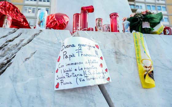 A handwritten sign with prayers for Pope Francis’ recovery is seen among candles and flowers at the base of a statue of St. John Paul II outside Rome’s Gemelli hospital Feb. 27, 2025. The pope has been hospitalized there since Feb. 14. (CNS/Lola Gomez)