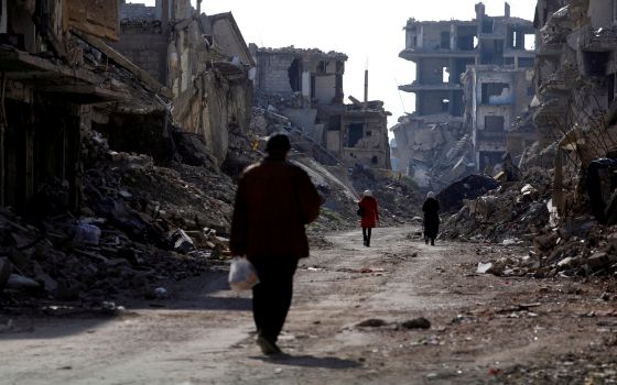 People walk past damaged buildings at the Yarmouk Palestinian refugee camp on the outskirts of Damascus, Syria Dec. 2, 2020.(CNS/Reuters/Omar Sanadiki)