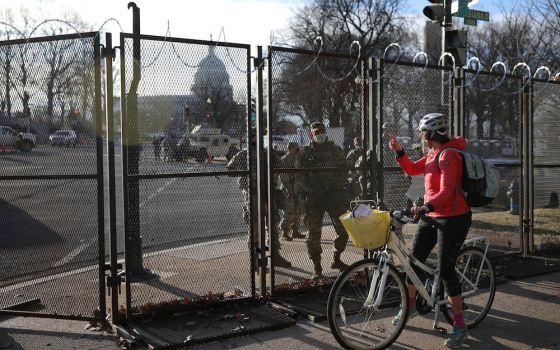 The U.S. Capitol can be seen behind the protective fence line Jan. 21, 2021, as a cyclist talks to a U.S. National Guard member inside. (CNS/Reuters/Tom Brenner)