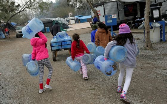 Children carry empty water containers inside a migrant encampment in Matamoros, Mexico, Feb. 18, 2021. (CNS/Reuters/Daniel Becerril)