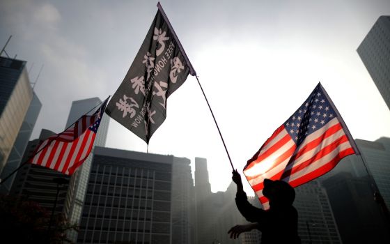 people waving US flags and a flag with Chinese writing seen against buildings