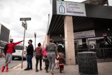 The sister stands in front of building as people filter in. 