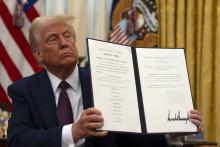 Trump sits holding up document. 