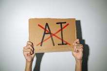 Hands holding a cardboard sign with the letters AI crossed out (Dreamstime/Wachiwit)